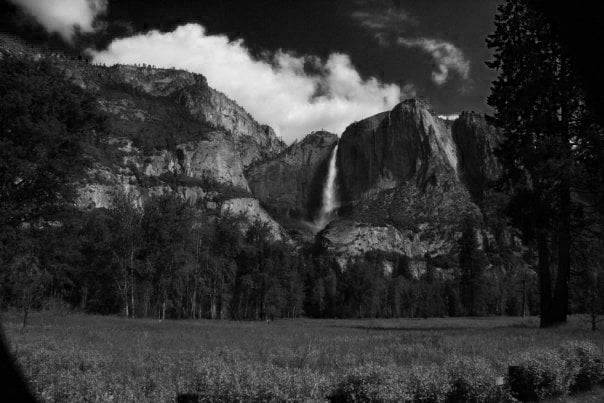 Yosemite Falls cascades from the granite cliffs, framed by towering pines and an open meadow below. Captured in black and white, the scene feels timeless — nature’s power and stillness balanced in a single frame.